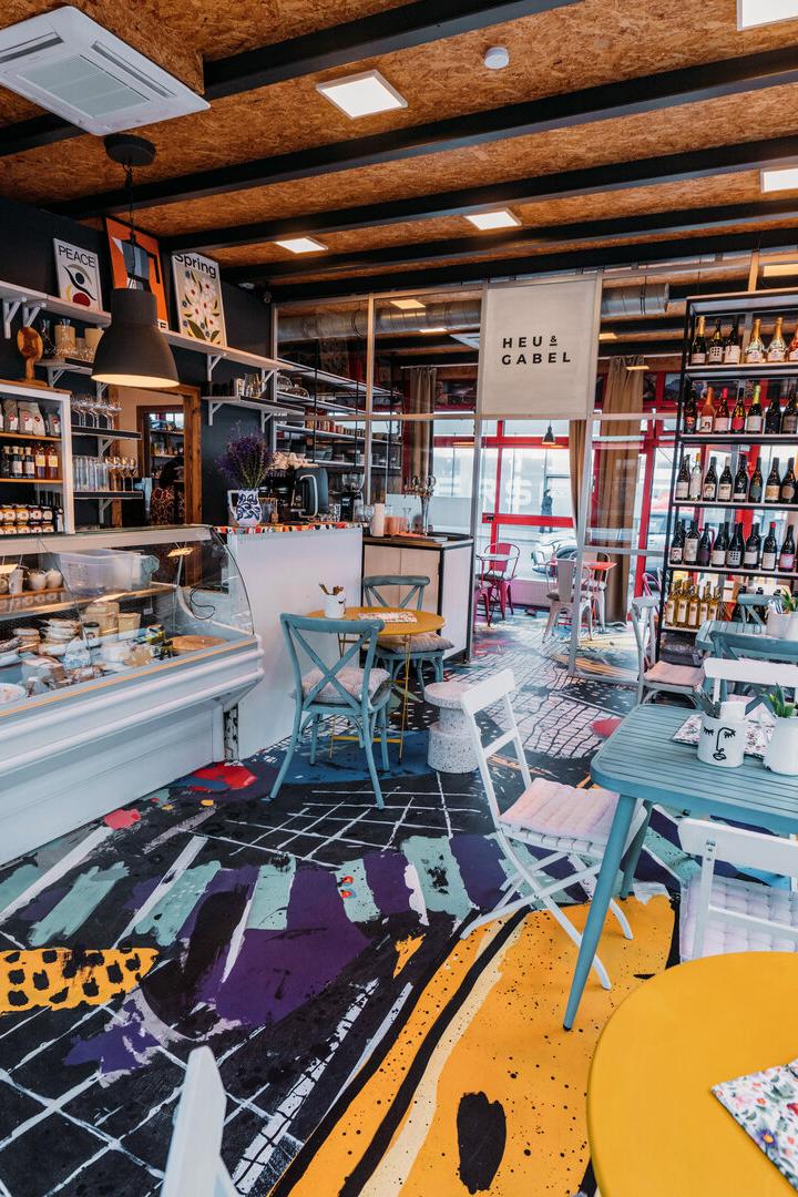 Innenansicht eines Feinkostladens mit Tischen und Regalen voller Produkte.