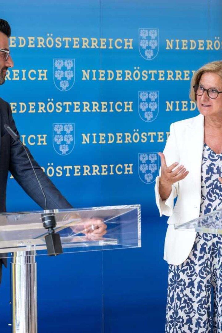 Ein Mann und eine Frau stehen an Rednerpulten vor einem Hintergrund mit dem Wappen von Niederösterreich.