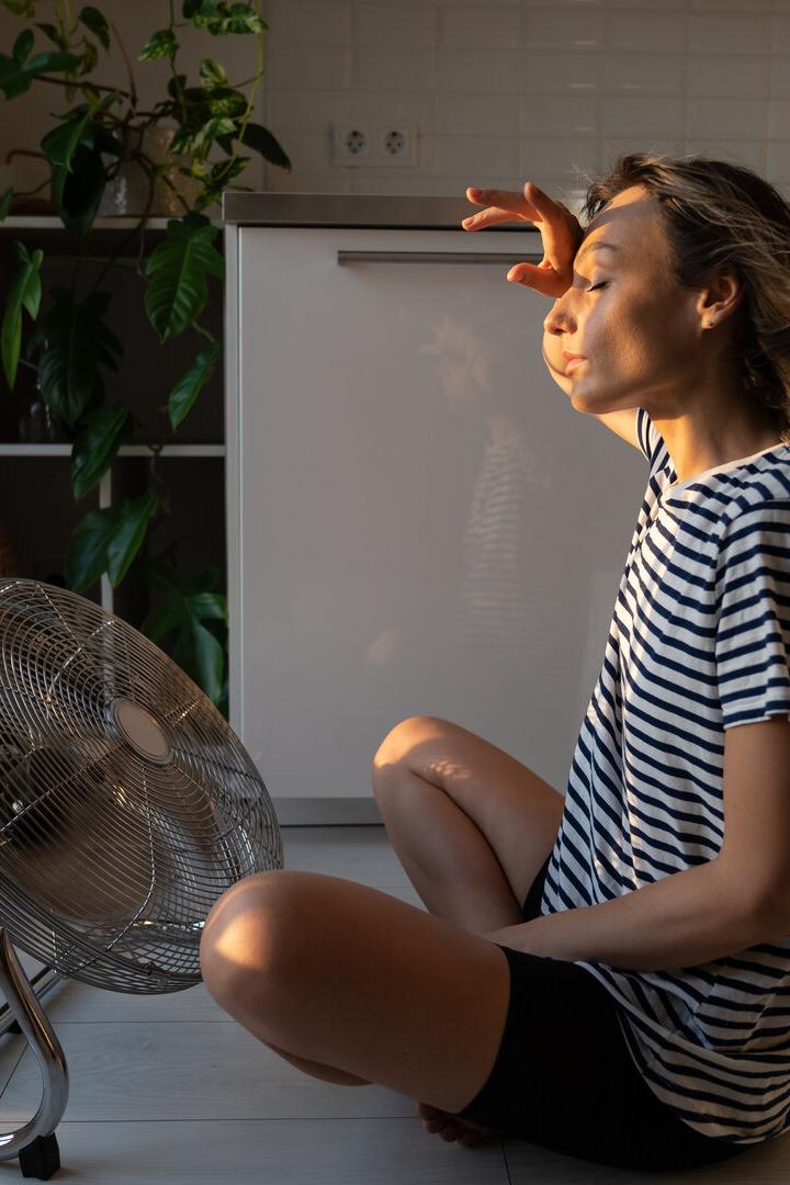 Frau sitzt vor einem großen Ventilator. 