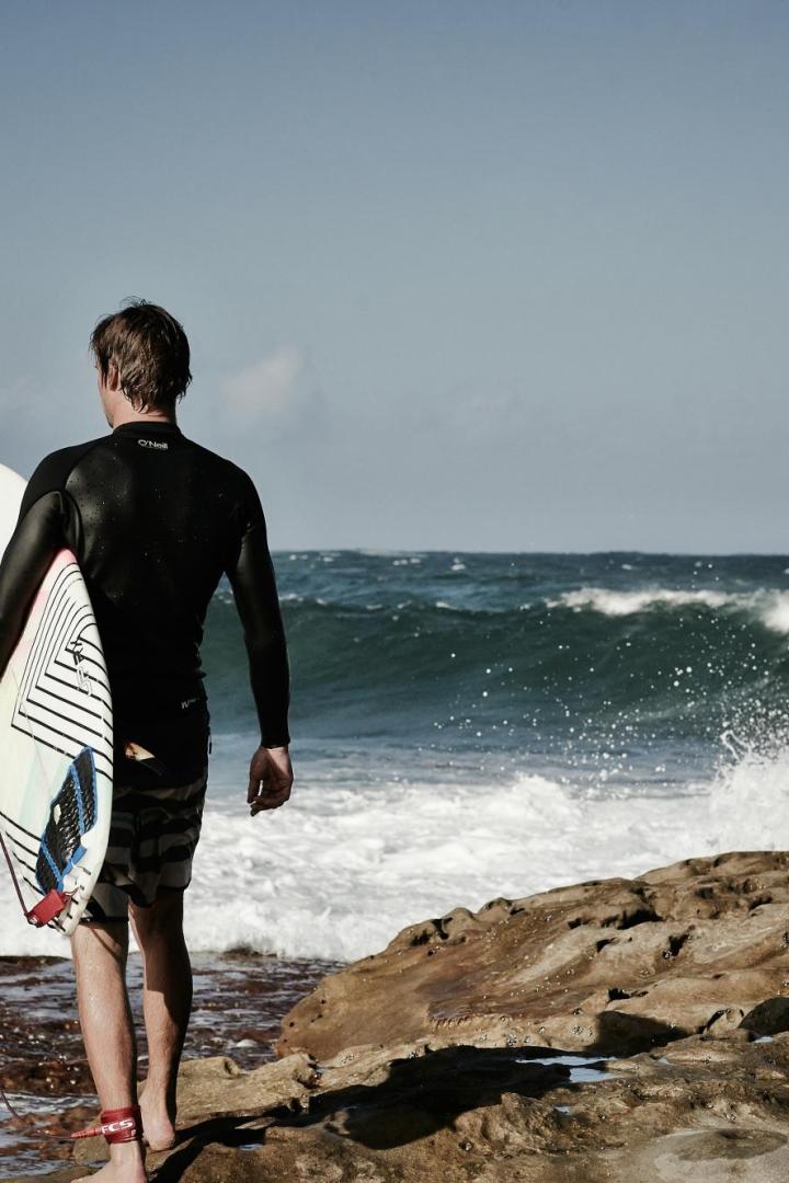 Surfer mit Brett geht auf Wasser zu