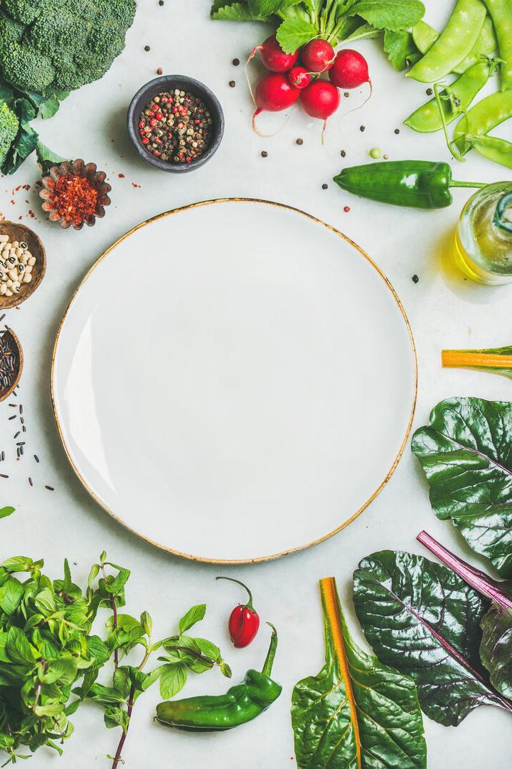 Fresh greens, vegetables and grains with white plate in center