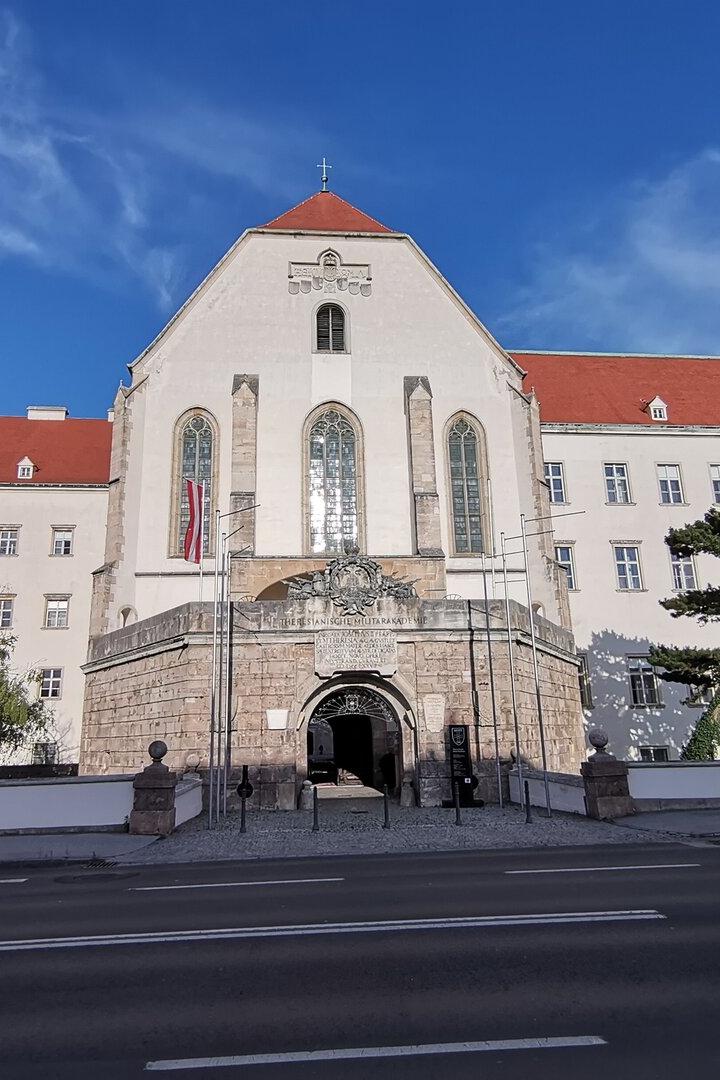 Große historische Klosteranlage mit rotem Dach und Torbogen vor blauem Himmel.