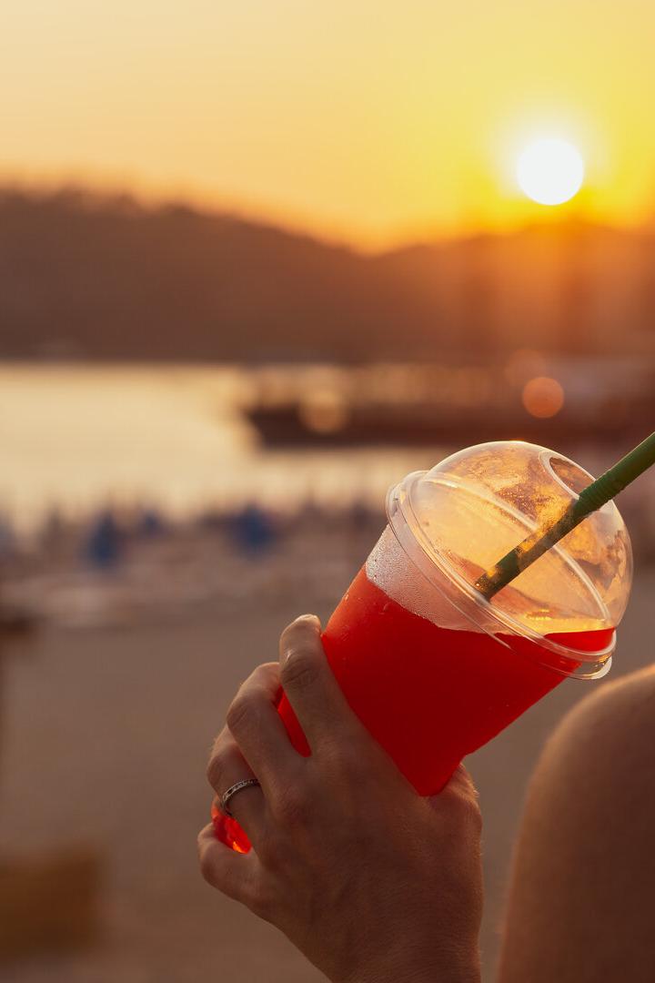 Eine junge Frau schlürft genüsslich einen Slushie im Sonnenuntergang an einem Seeufer