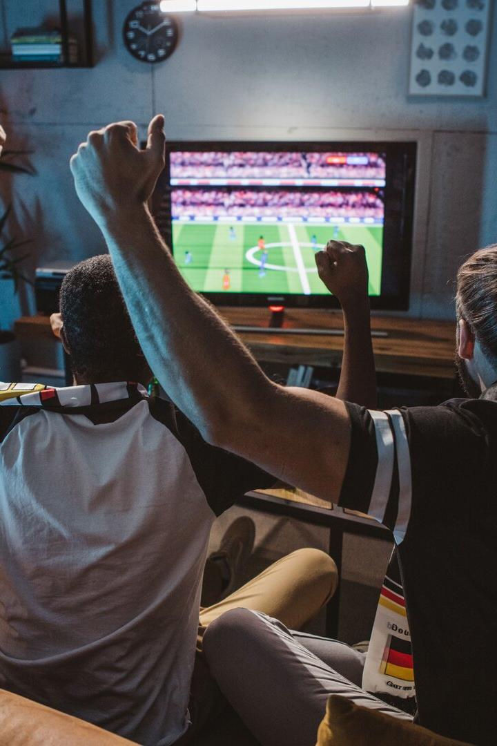 Fußballfans sitzen gemeinsam vor dem Fernseher und jubeln.
