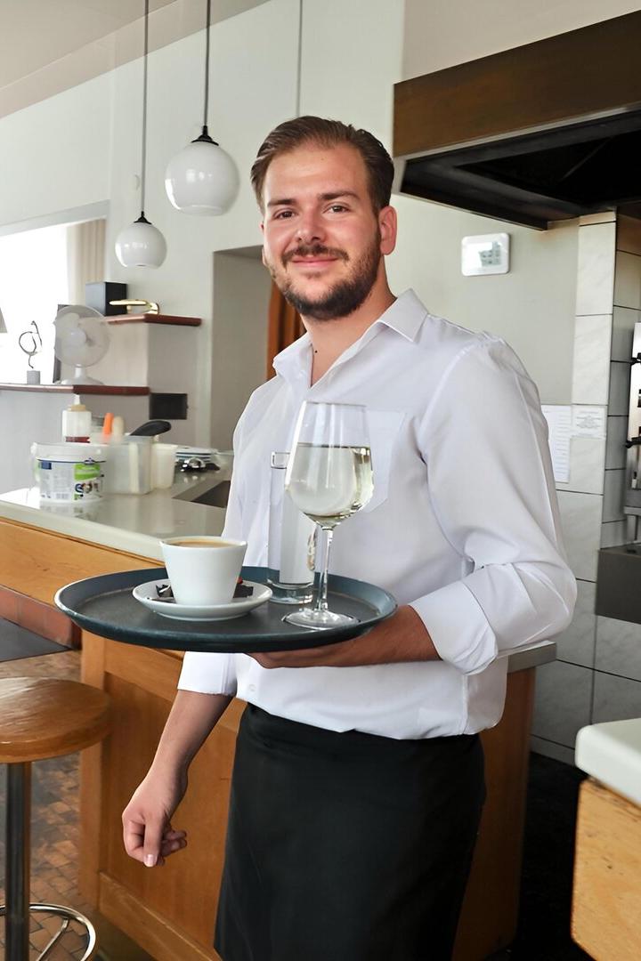 Ein Kellner mit einem Tablett mit Kaffee und einem Glas Wein in einem Restaurant.
