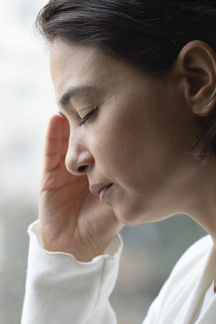 Frau mit geschlossenen Augen hält sich die Schläfe und wirkt nachdenklich oder erschöpft.