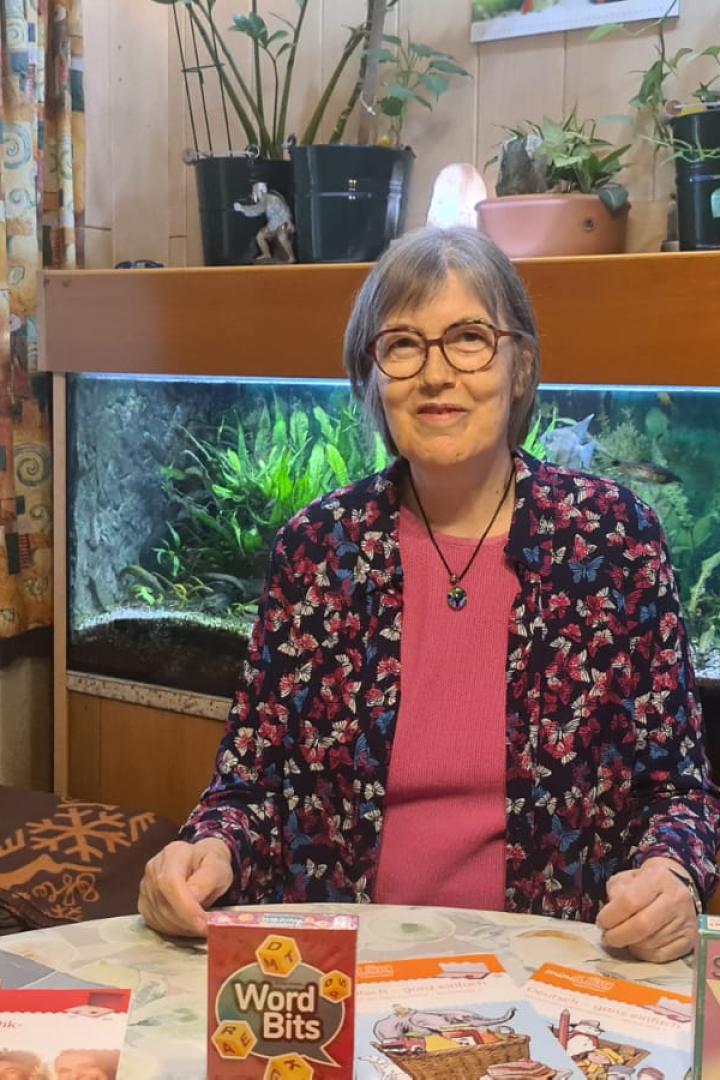 Christa Teitzer sitzt an einem Tisch vor einem Aquarium, auf dem mehrere Spiele zu sehen sind.