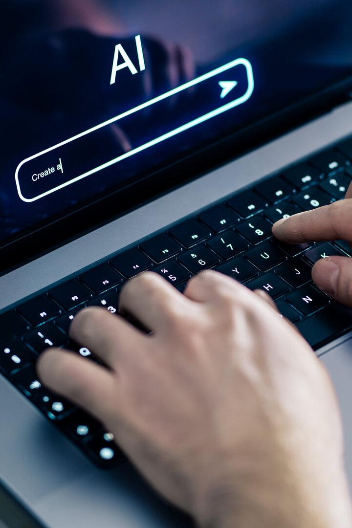 Hände tippen auf einer Laptop-Tastatur, auf dem Bildschirm steht „AI“ mit einer Suchleiste.