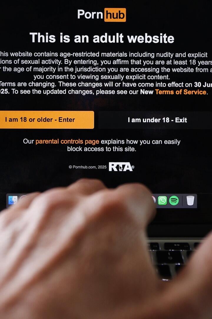 Auf einem Laptop-Bildschirm ist die Altersabfrage von Pornhub zu sehen. Eine Hand berührt die Tastatur.