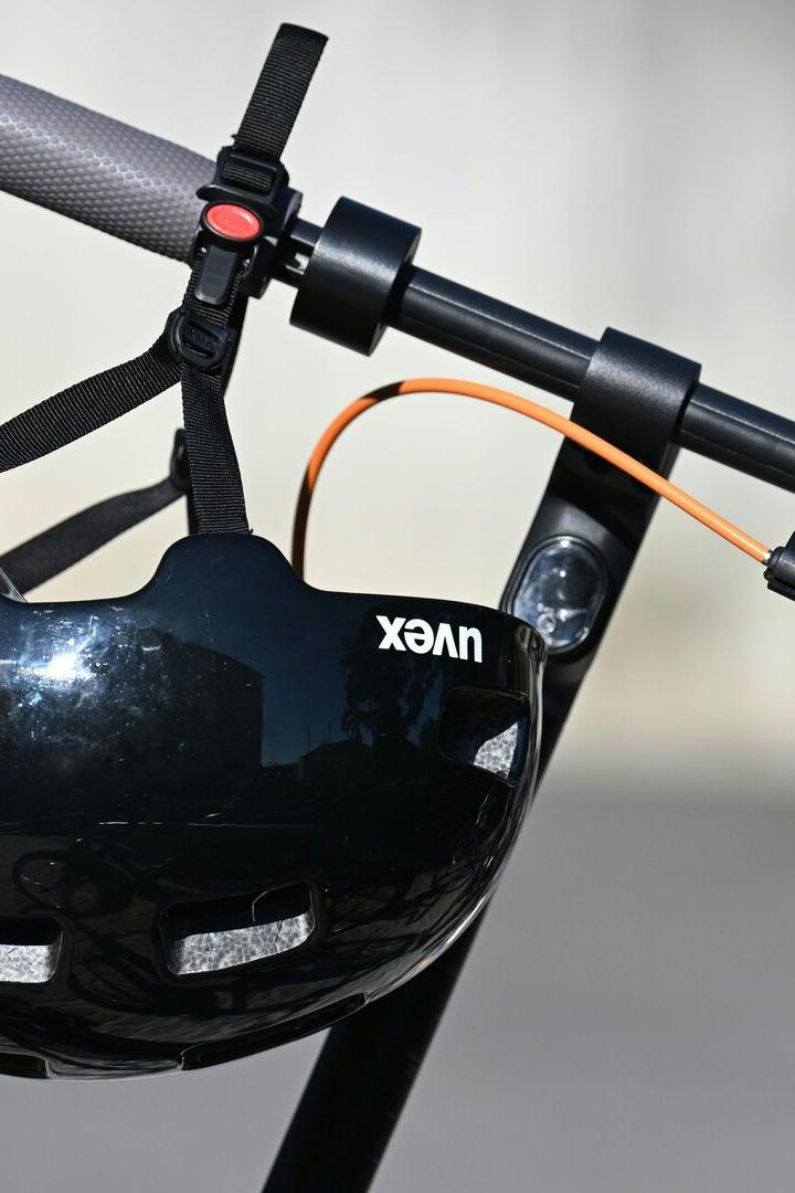 Ein schwarzer Fahrradhelm hängt am Lenker eines E-Scooters mit grauen Griffen und orangefarbenem Kabel.