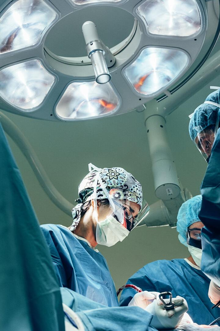 Ein OP-Team in blauer Kleidung arbeitet unter hellem Licht im Operationssaal.