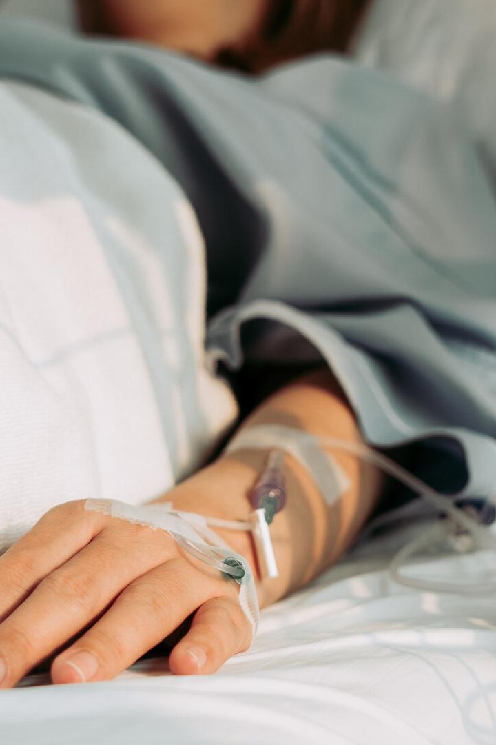Eine Person liegt im Krankenhausbett, ein Infusionsschlauch ist an ihrem Arm befestigt.