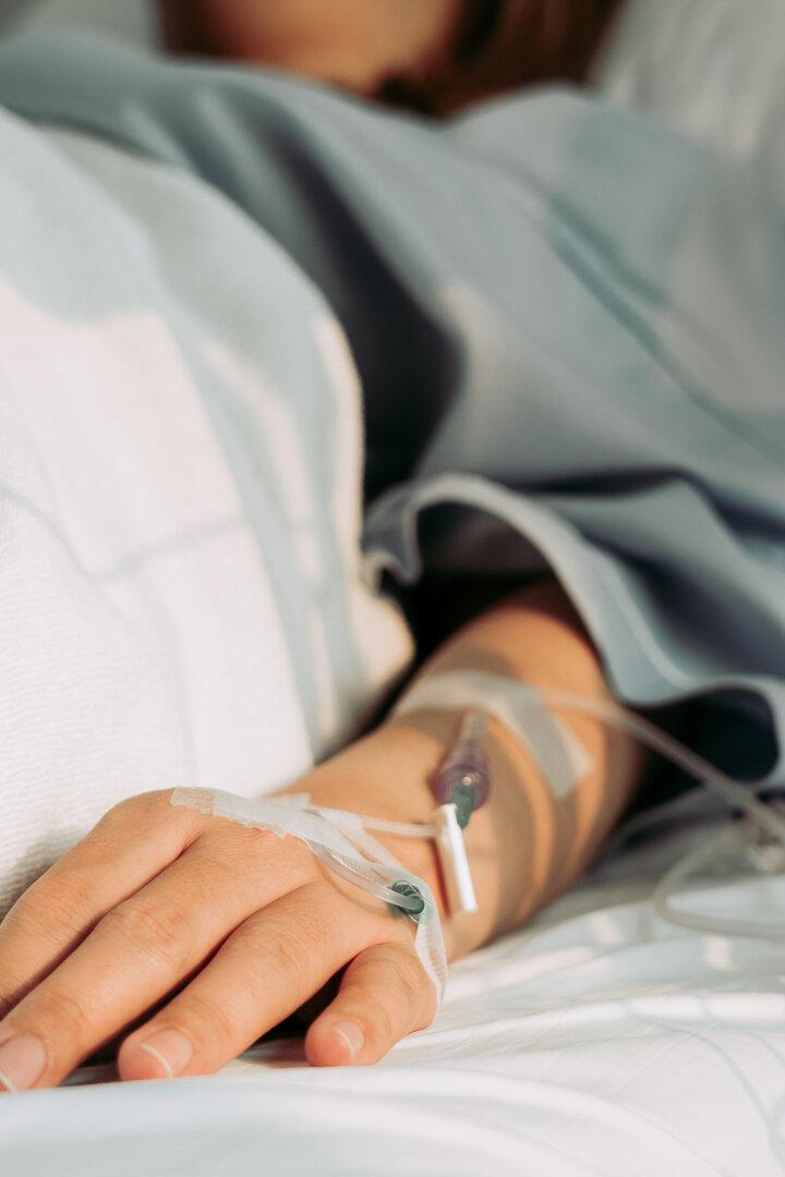 Eine Person liegt im Krankenhausbett, ein Infusionsschlauch ist an ihrem Arm befestigt.