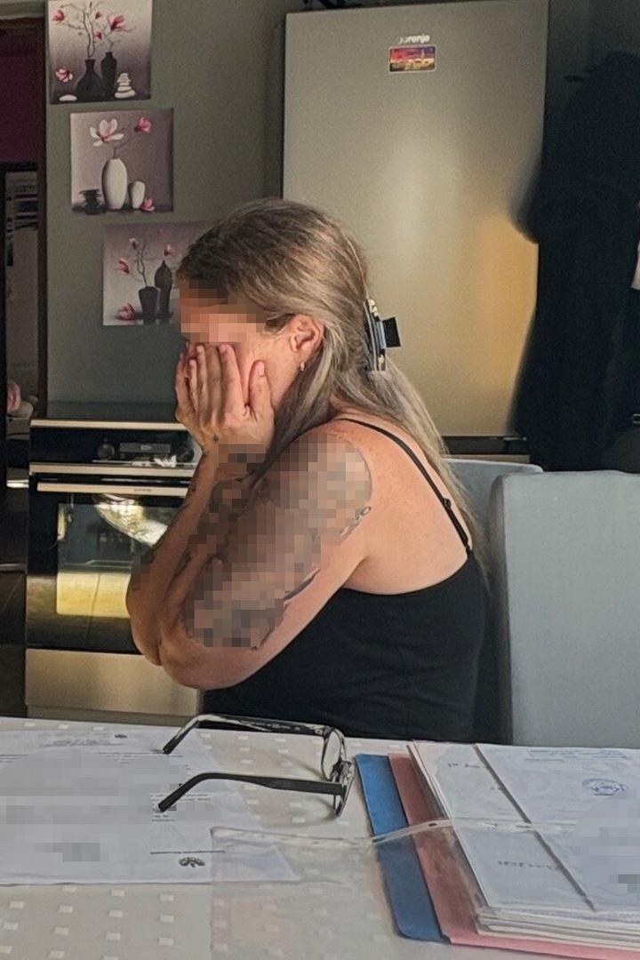 Eine Frau mit Tätowierung sitzt verzweifelt an einem Tisch mit Dokumenten.