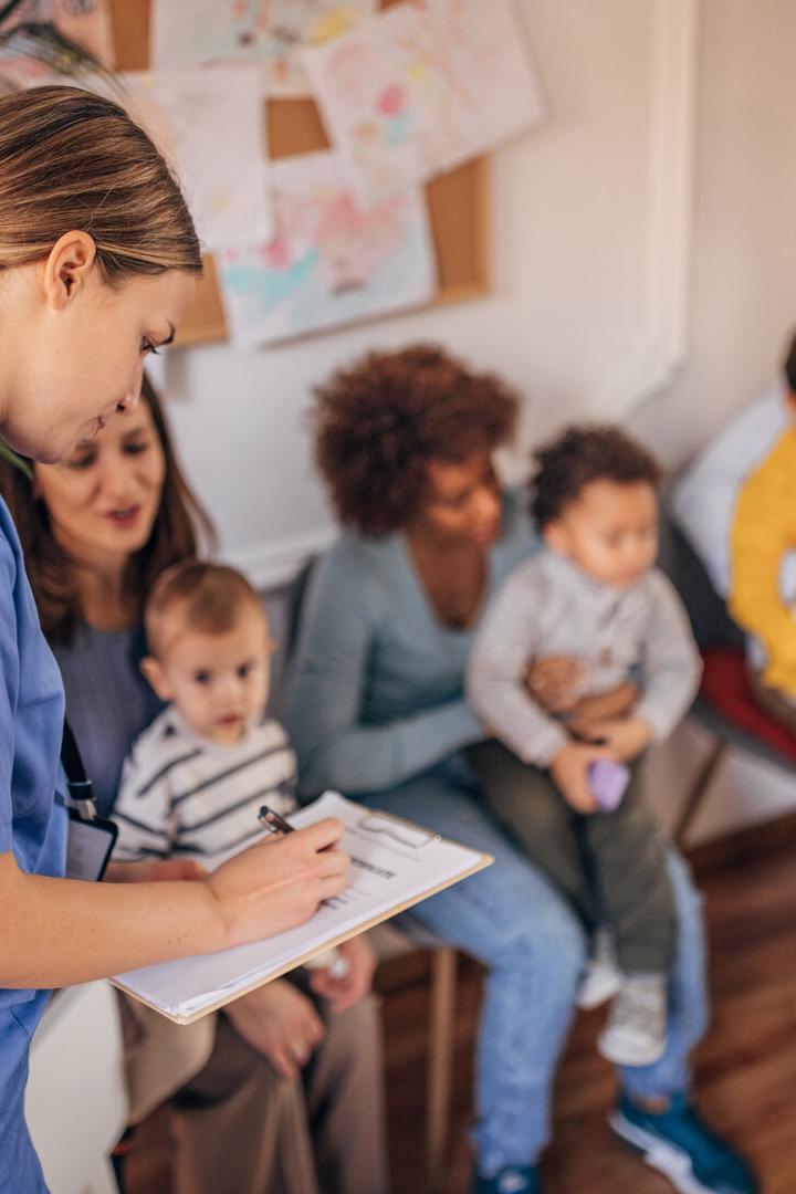 Eine Krankenschwester macht sich Notizen, während Familien mit Kindern im Wartezimmer sitzen.
