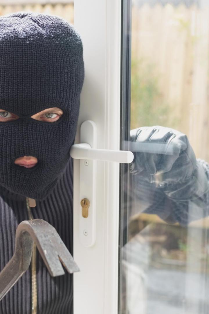 Eine maskierte Person mit Brecheisen versucht, eine Terrassentür aufzubrechen.