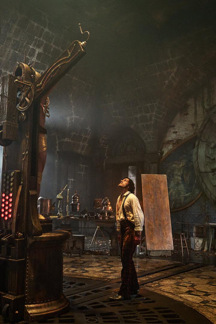 Filmszene: Victor Frankenstein steht in seinem Labor und sieht auf seine Kreatur, die auf einem Kreuz aufgepannt ist.