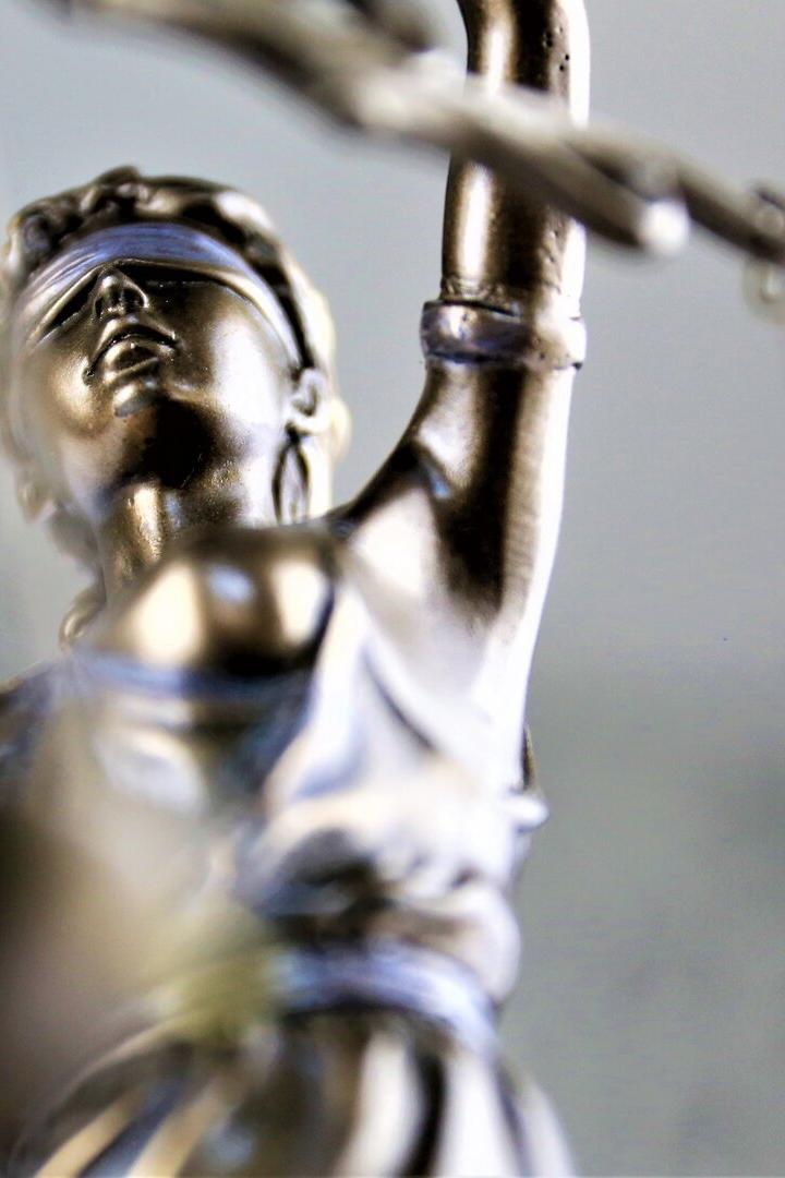 Eine silberne Justitia-Figur mit verbundenen Augen hält eine Waage in der erhobenen Hand.