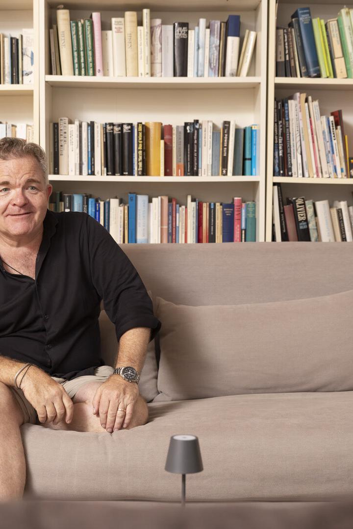 Cornelius Obonya sitzt lässig auf einer Couch vor seinem Bücherregal.