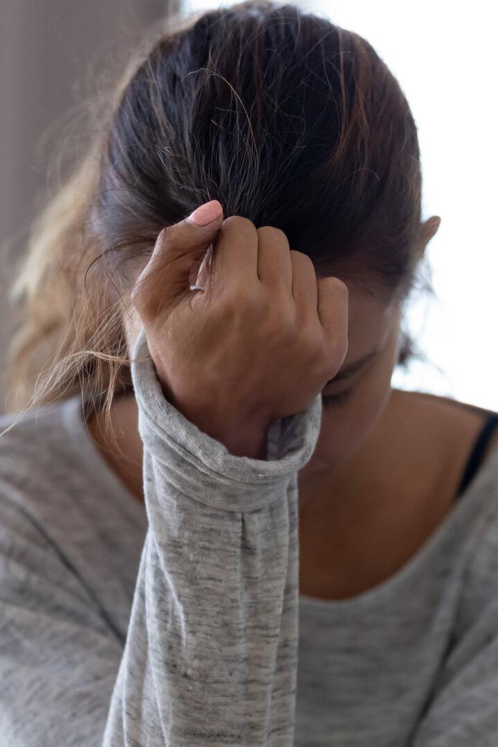 Eine Frau sitzt mit gesenktem Kopf und hält sich die Stirn, wirkt nachdenklich oder besorgt.