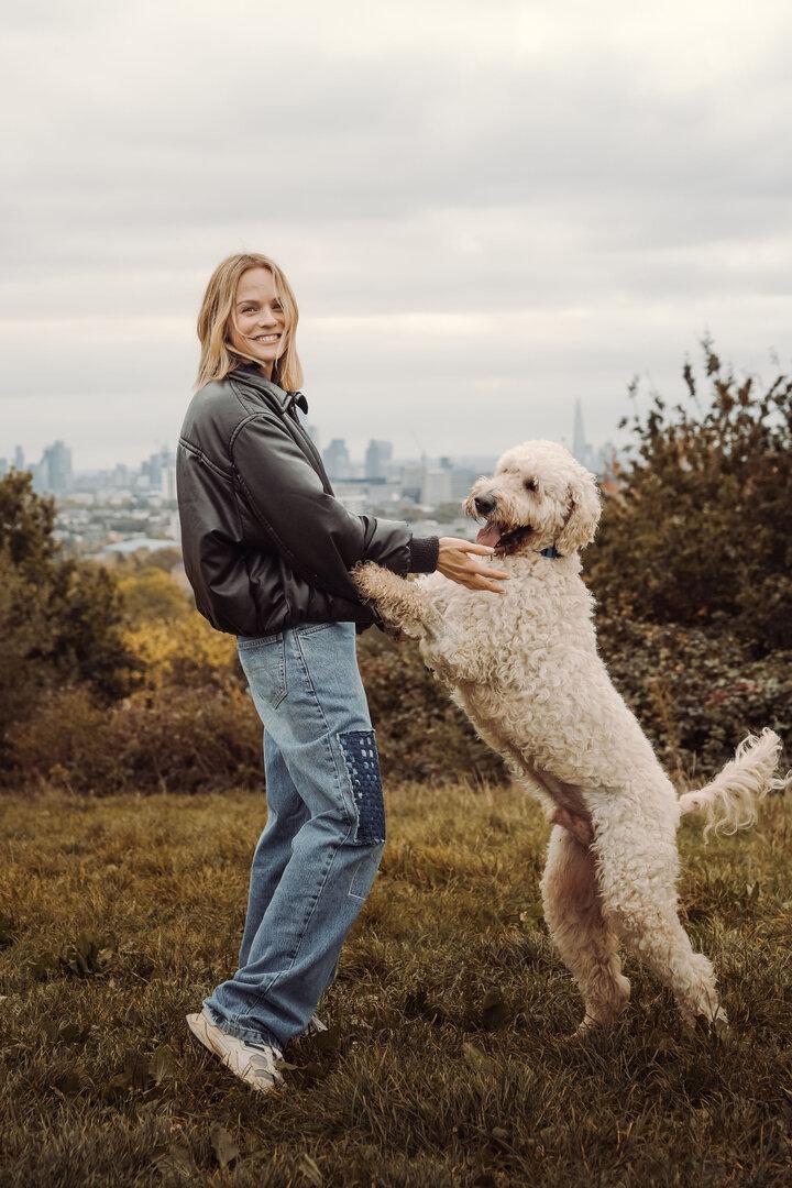 Ein beiger, wuscheliger Hund, wie er mit Moderatorin Mirjam Weichselbraun auf einer Wiese spielt