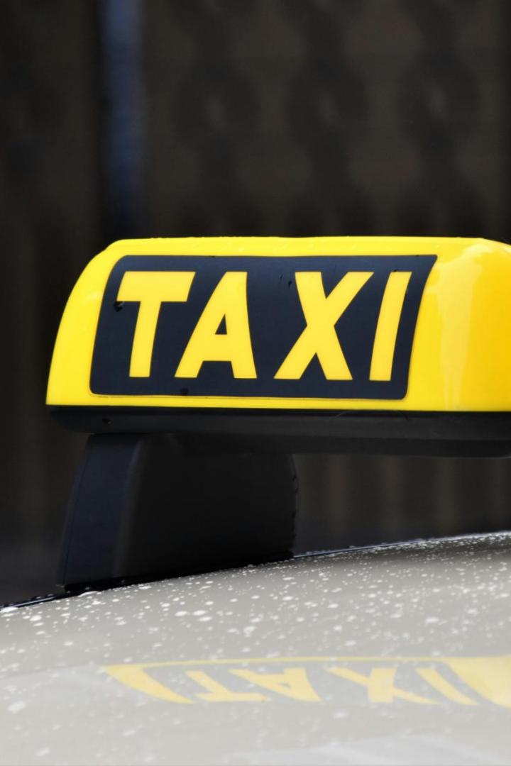 Gelbes TAXI-Dachzeichen auf einem Auto, im Hintergrund unscharf.