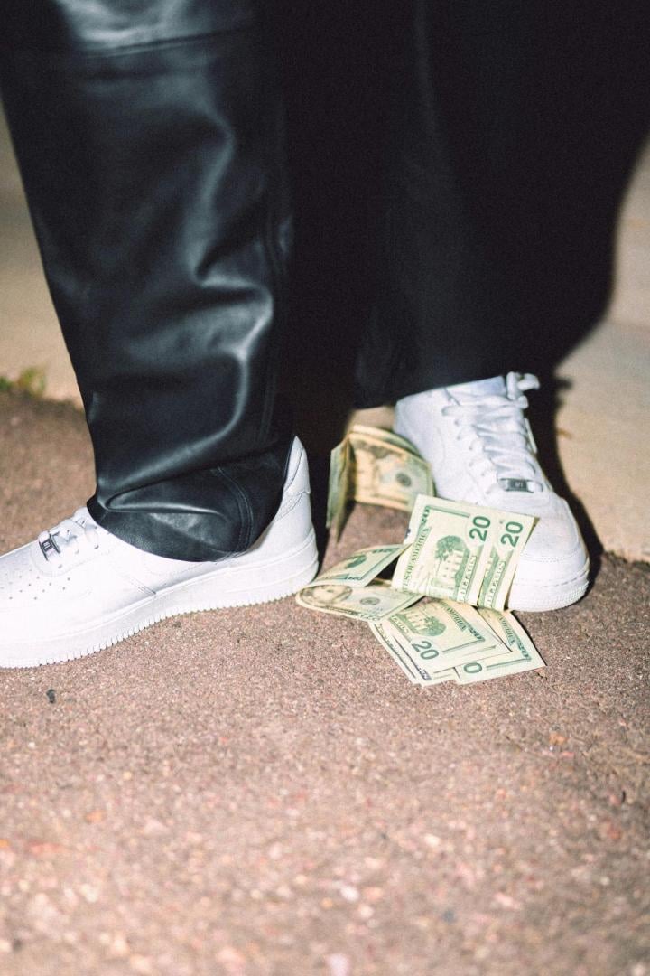Weiße Sneaker steigen auf Geldscheine drauf.