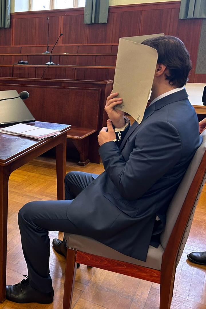 Angeklagter verdeckt vor Gericht sein Gesicht mit einer Mappe