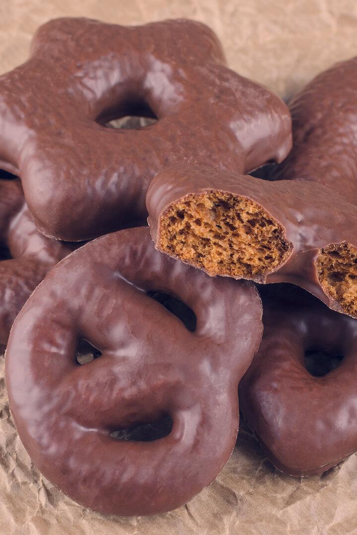 Mehrere mit Schokolade überzogene Lebkuchen in verschiedenen Formen liegen auf braunem Papier, daneben Zimtstangen und Sternanis.