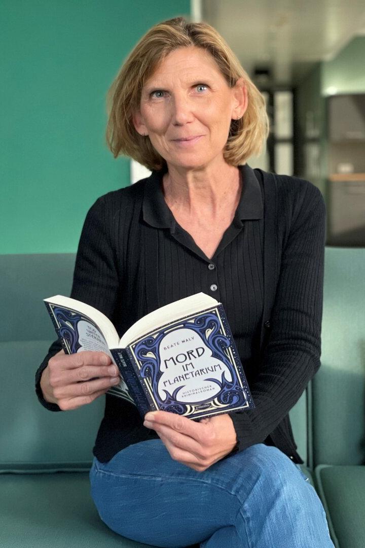 Beaty Maly sitzt auf einer Couch und blättert in ihrem neuen Buch