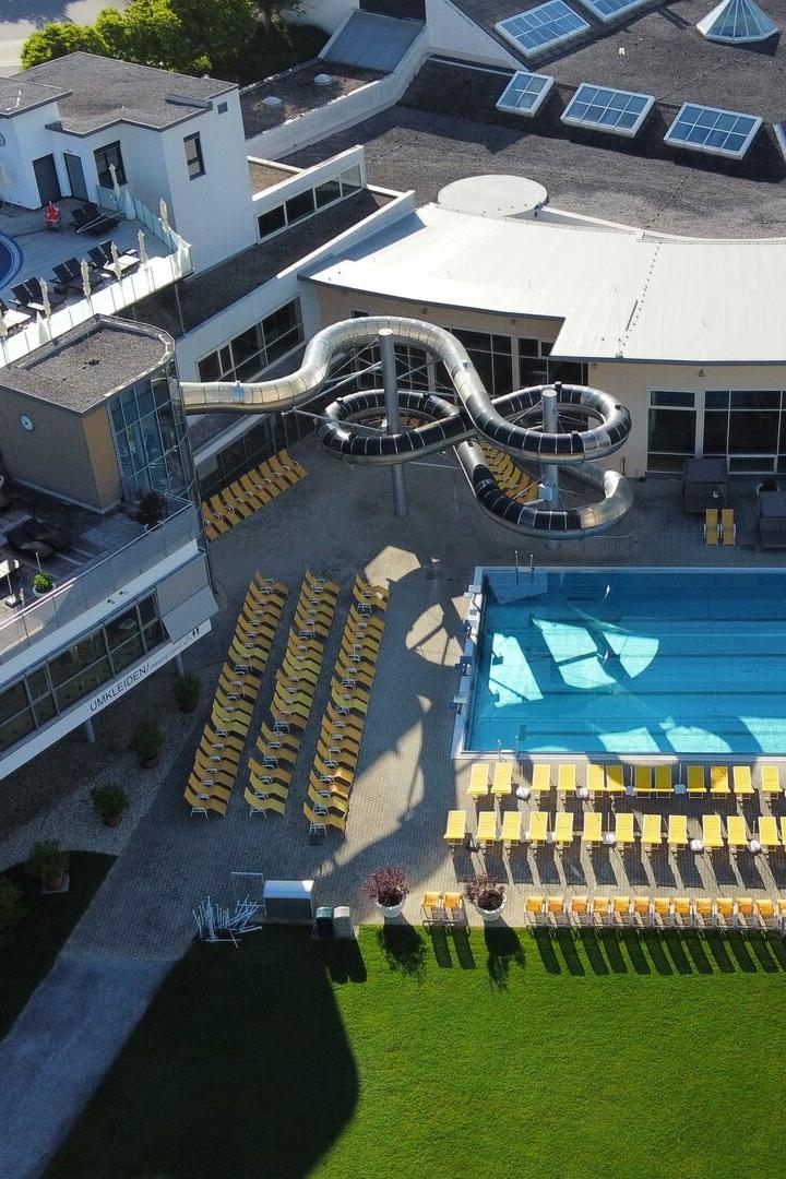 Draufsicht auf ein Schwimmbad mit Liegestühlen, Rutsche und dem Schriftzug "Allegria" auf einem Gebäude.