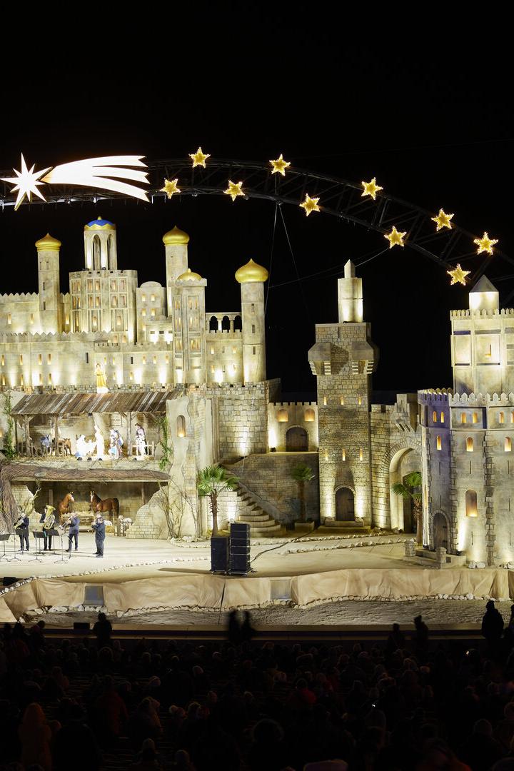 Bühnenbild mit hell beleuchteten, turmähnlichen Strukturen und einer Sternenbogen-Dekoration mit einem leuchtenden Kometen darüber.