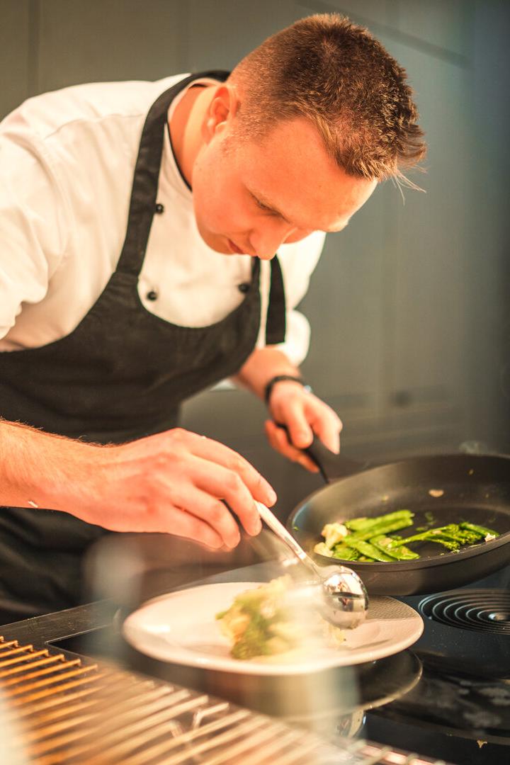 Ein Koch richtet konzentriert mit einer Kelle Gemüse aus einer Pfanne auf einem Teller an.