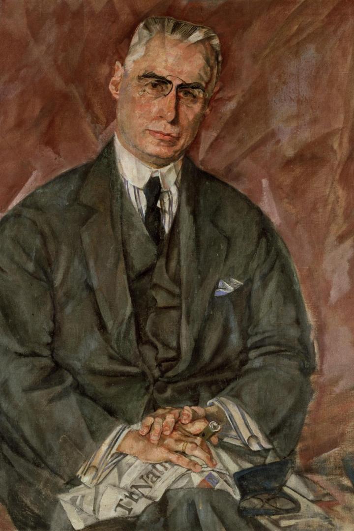 Porträt eines sitzenden Mannes in dunklem Anzug mit Krawatte, die Hände gefaltet auf einer Zeitung und einem geöffneten Etui auf dem Schoß.