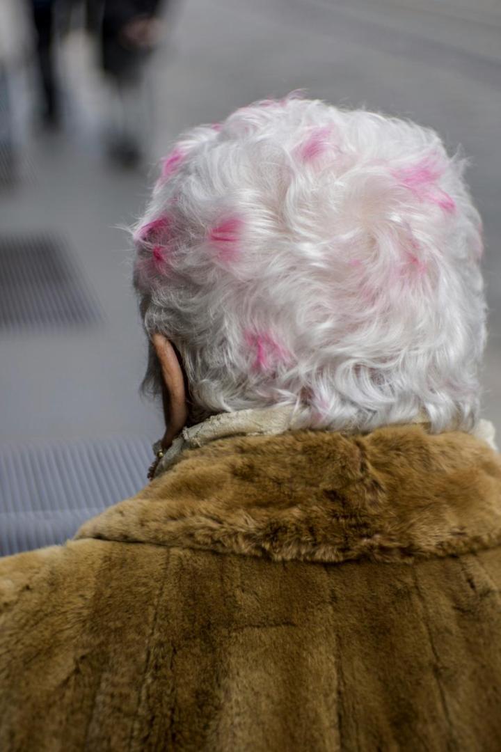 Eine ältere Person mit weißem Haar und rosa Akzenten trägt einen braunen Pelzmantel.