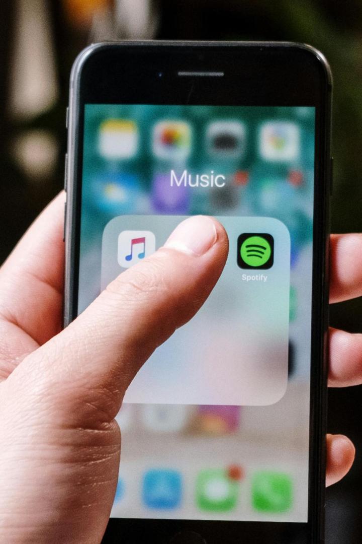Hand hält Smartphone mit geöffnetem Musik-Ordner und sichtbarem Spotify-Icon.