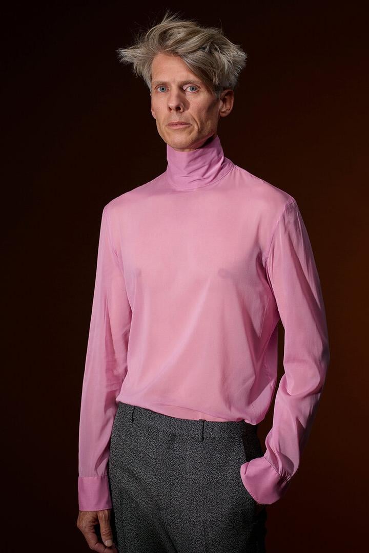 Ein blonder Mann in einem rosa Pulli
