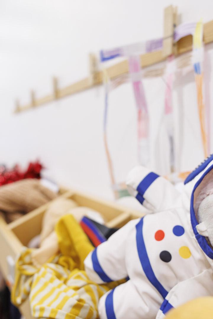 Ein rosa Kuscheltier im Astronautenanzug liegt auf einer Garderobe mit bunten Bändern und Kleidung.