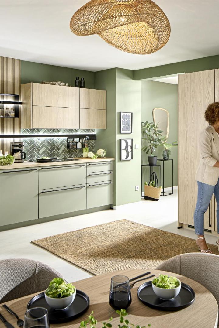 Moderne Küche mit grünen und Holzelementen, eine Frau nimmt ein Glas aus einem offenen Vorratsschrank.