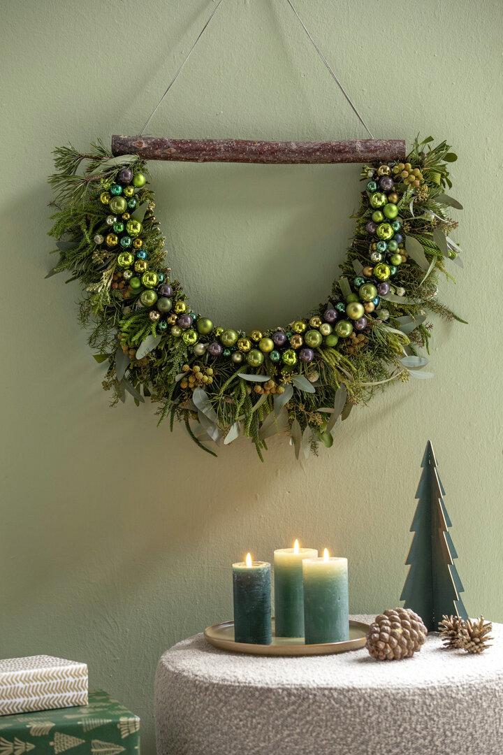 Dekorative Girlande: Tannenzweige werden mit glänzenden Kugeln in Grüntönen kombiniert, das ganze auf einem stabilen Ast befestigt. 