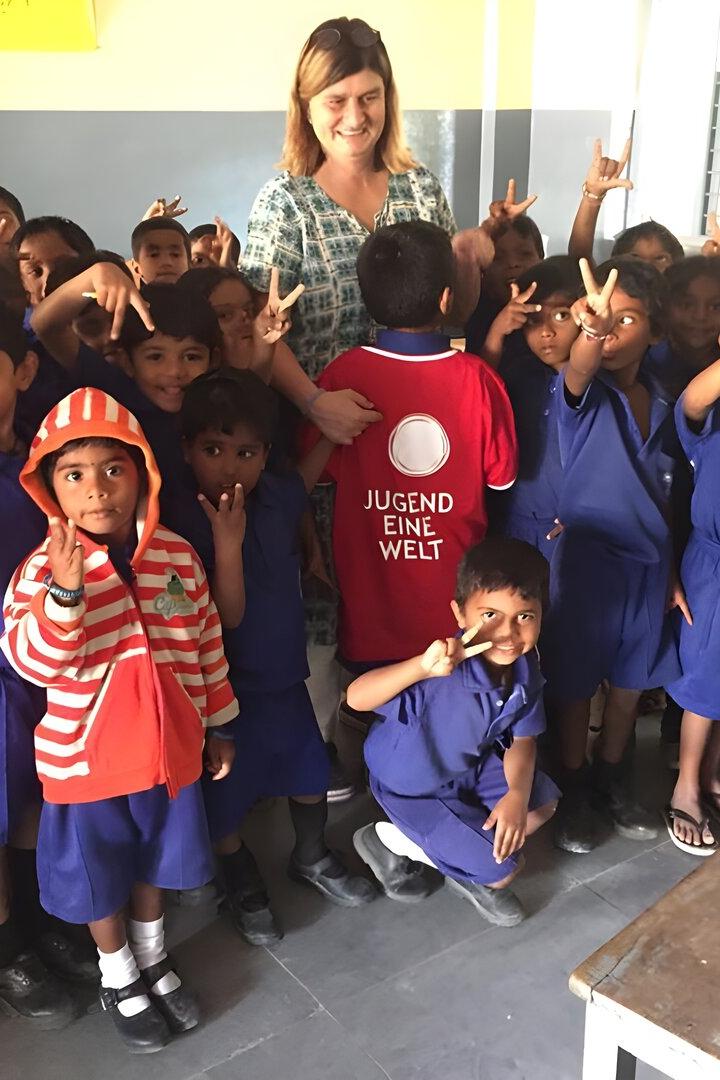 Eine Gruppe Kinder in blauen Schuluniformen posiert mit einer Frau und einem Jungen mit "Jugend Eine Welt"-Shirt.
