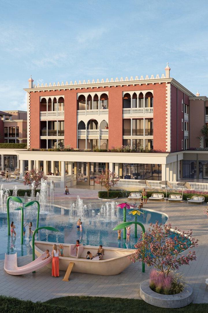 Vor einem großen, venezianisch wirkenden Gebäude entspannen Menschen auf Liegen und spielen Kinder in einem Pool mit Wasserspielen und Rutsche.