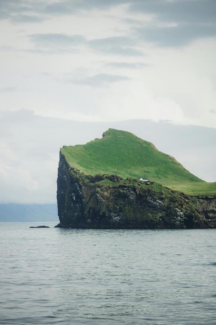 Weißes Haus steht einsam auf grüner Klippeninsel im Meer unter bewölktem Himmel.