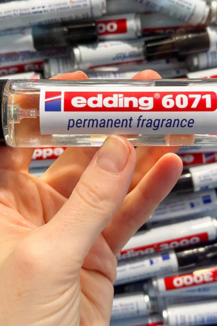 Eine Hand hält einen Flakon des limitierten Edding 6071 Parfums vor einem Hintergrund aus Edding-Markern.