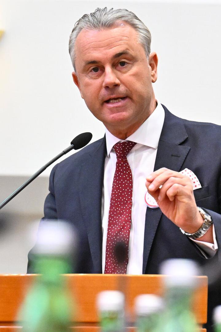 Ein Mann im Anzug spricht an einem Rednerpult mit Mikrofon, im Vordergrund stehen mehrere Flaschen.