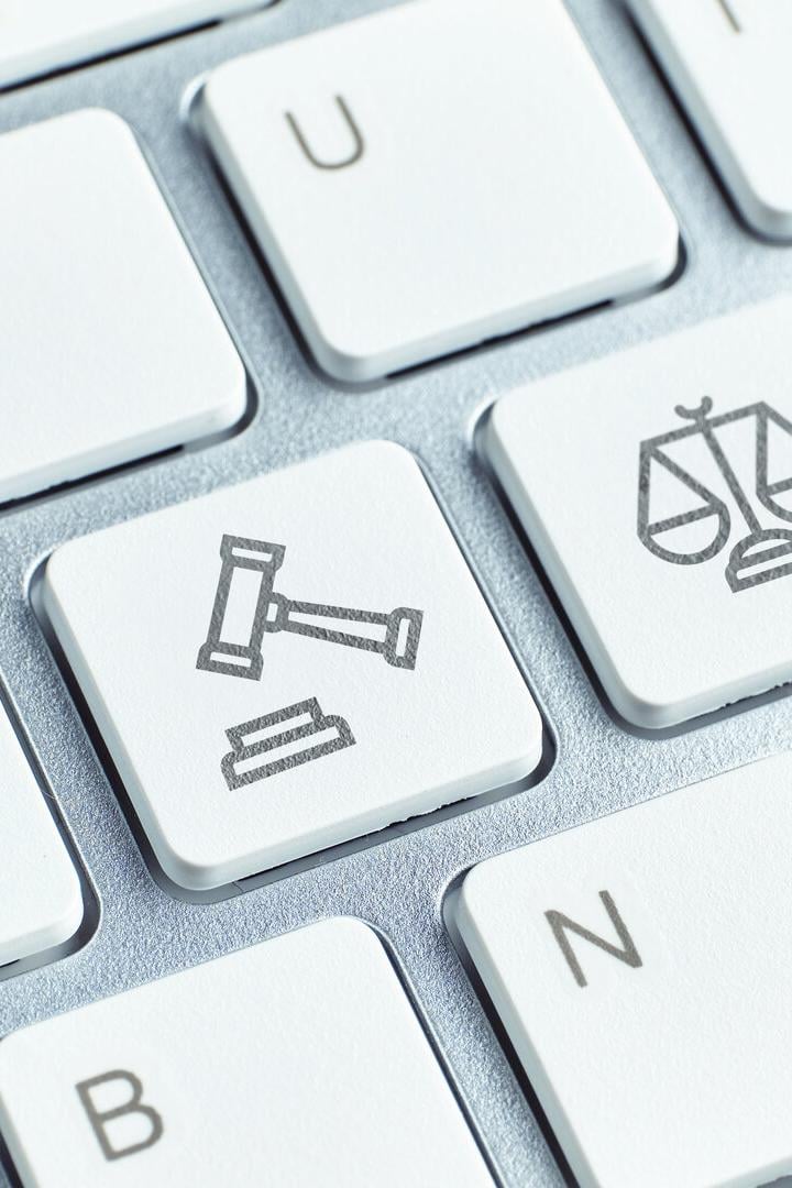 Eine kleine Figur steht auf einer Computertastatur mit Tasten, die Richterhammer und Waage zeigen.