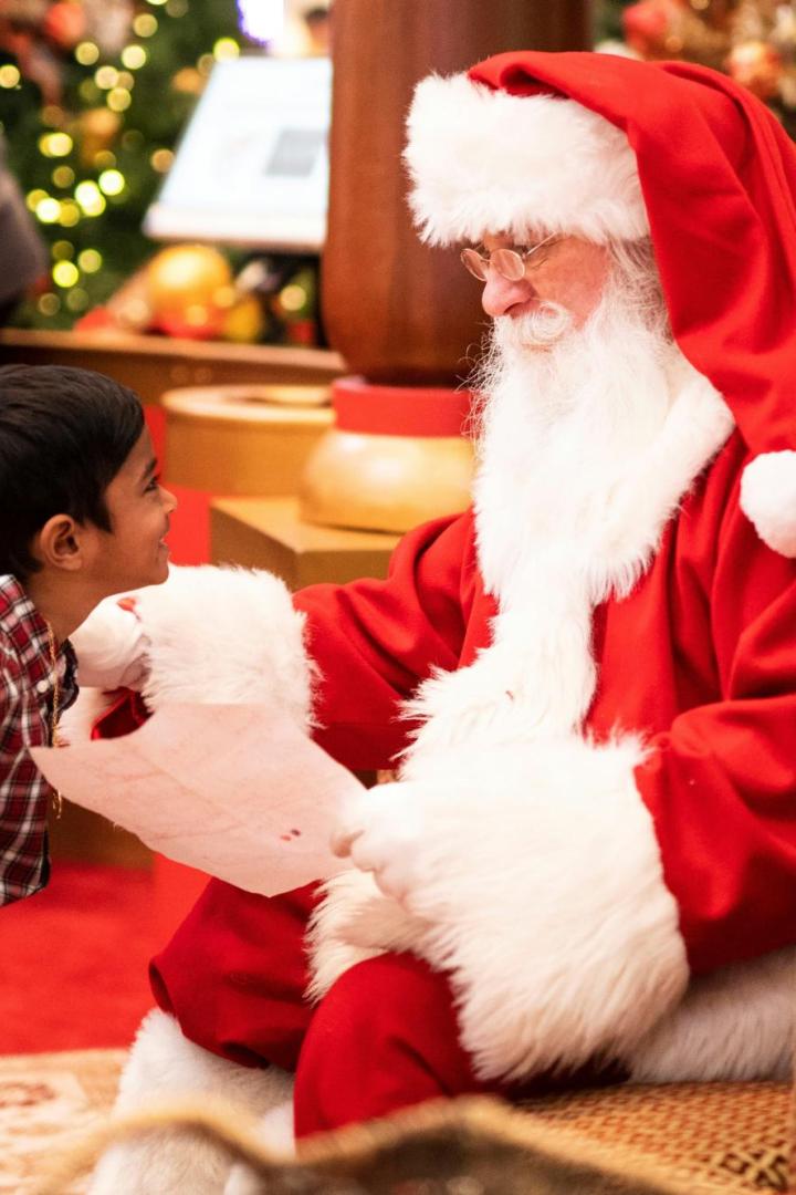 Ein Kind spricht lächelnd mit einem als Weihnachtsmann verkleideten Mann.