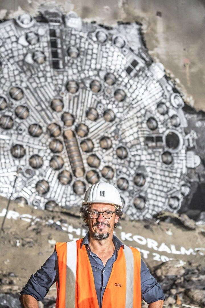 Ein Mann mit Bauhelm und in oranger Warnweste steht vor Tunnelbohrgerät