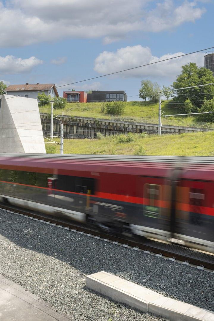 Roter Zug fährt an einem Tunnel und grünen Hügeln unter blauem Himmel vorbei.