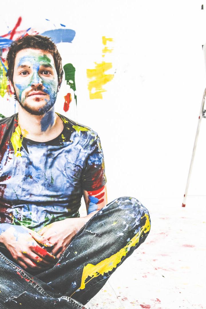 Eine farbige Darstellung eines Mannes, der nachdenklich am Boden sitzt, hinter ihm eine Wand mit Farbklecksen.